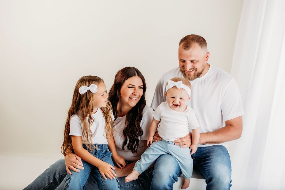Portrait of a happy family sitting together in a minimal white studio setting wearing casual outfits.