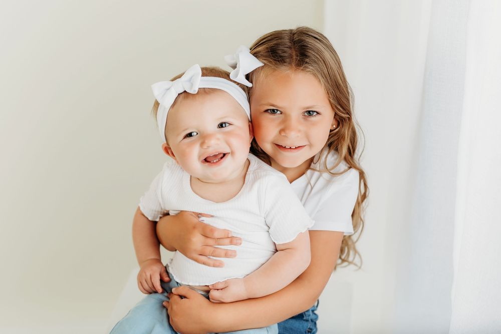 Children in casual outfits sharing sweet moments together against white backdrop.