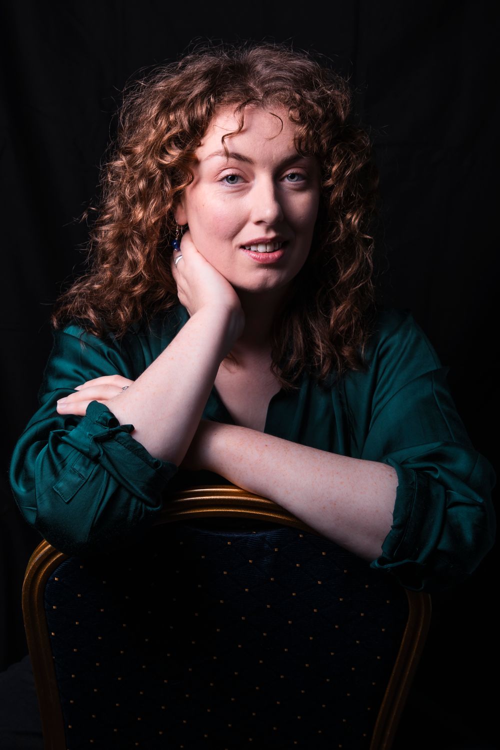 Portrait series of a redhead with curly hair in a dark green top against a black background.