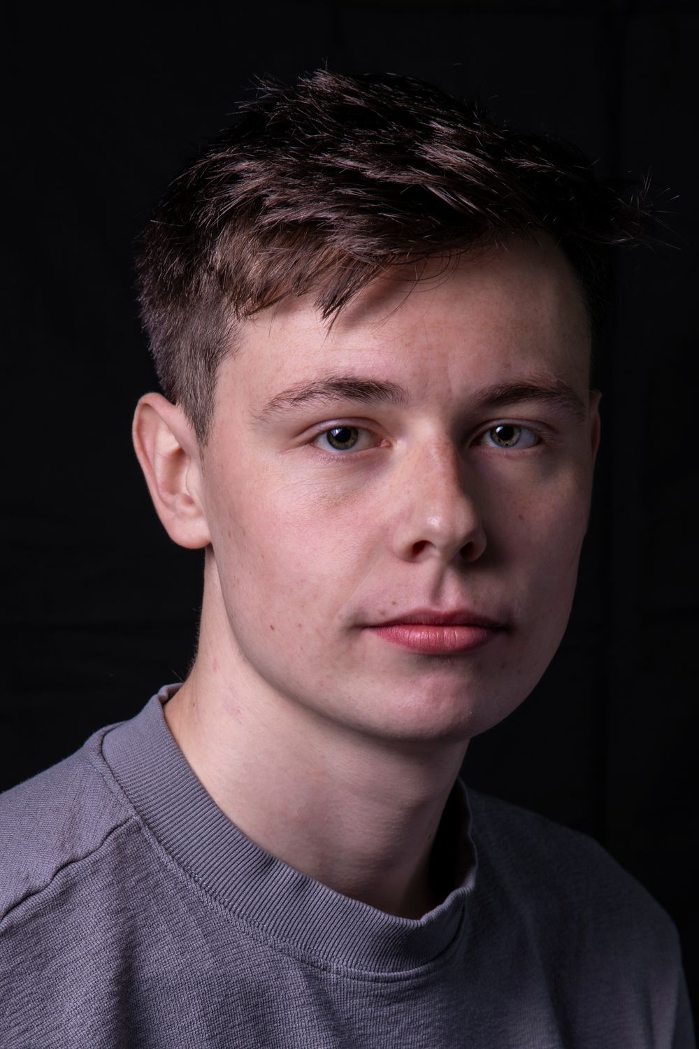 Portrait photo of a young person in a gray sweatshirt against a dark background with dramatic lighting.