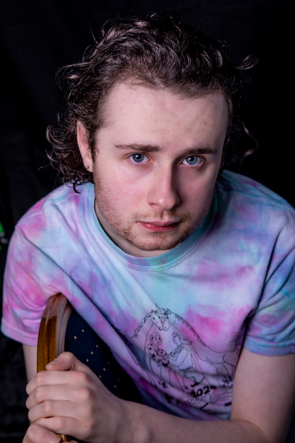 Someone wearing a tie-dye pink and purple t-shirt shown in a series of dark dramatic portraits.