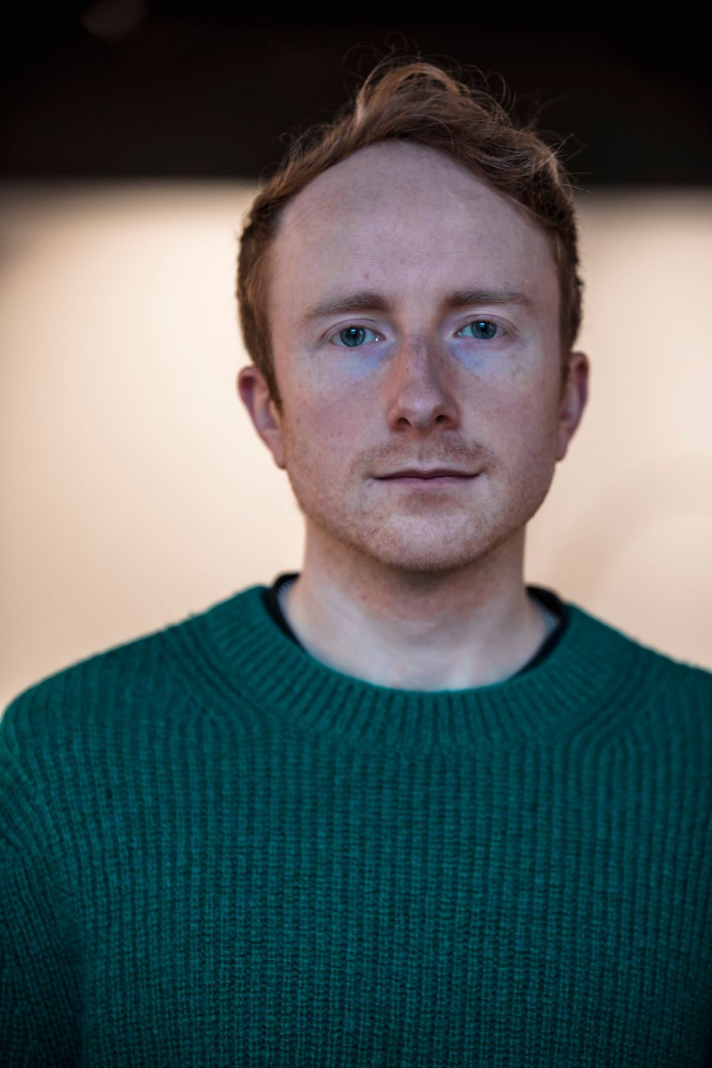 Young man with red hair and freckles wearing a green knit sweater, posing for a portrait photo.