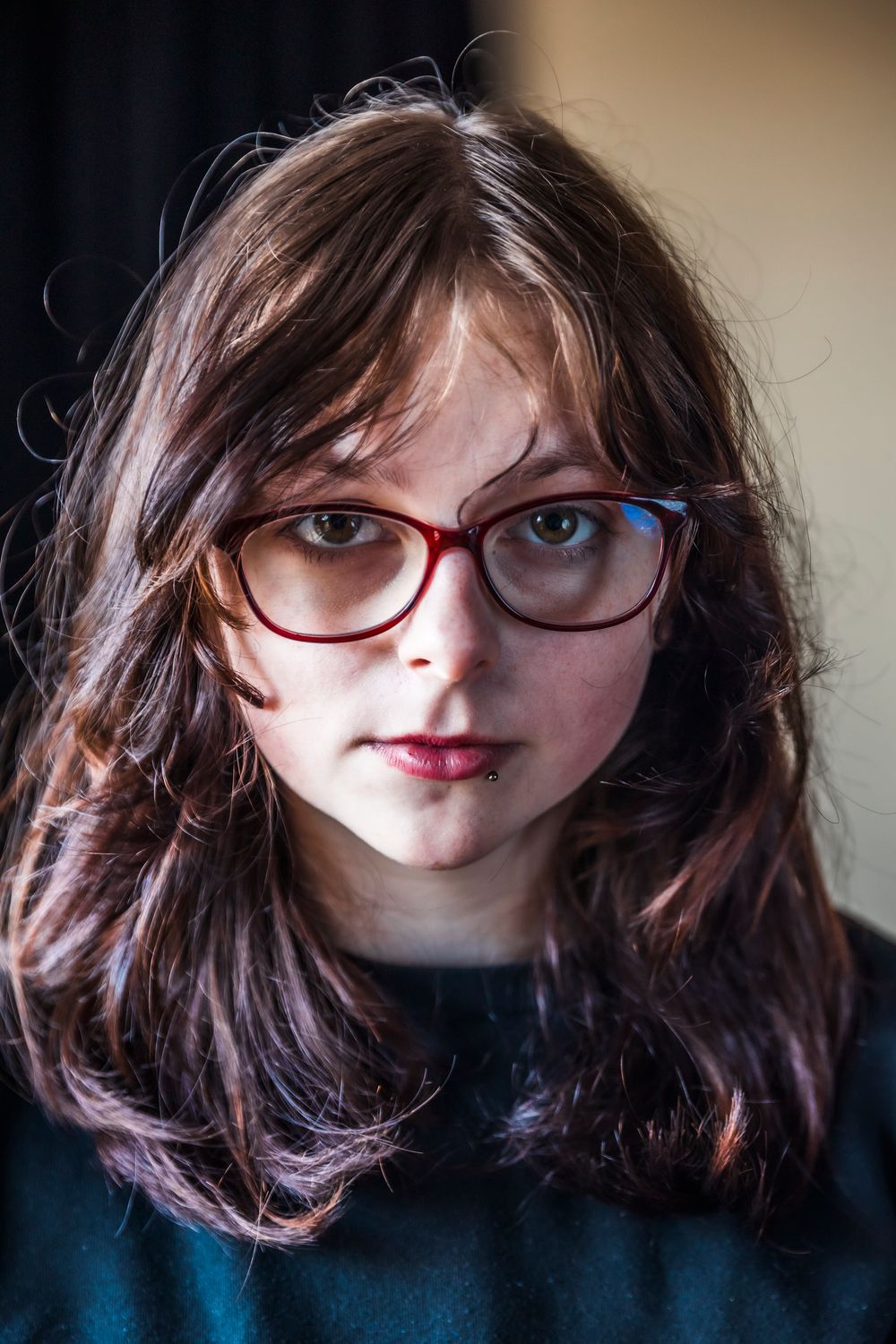 Young woman with long brown hair and red glasses looking directly at camera in a close-up portrait photo.