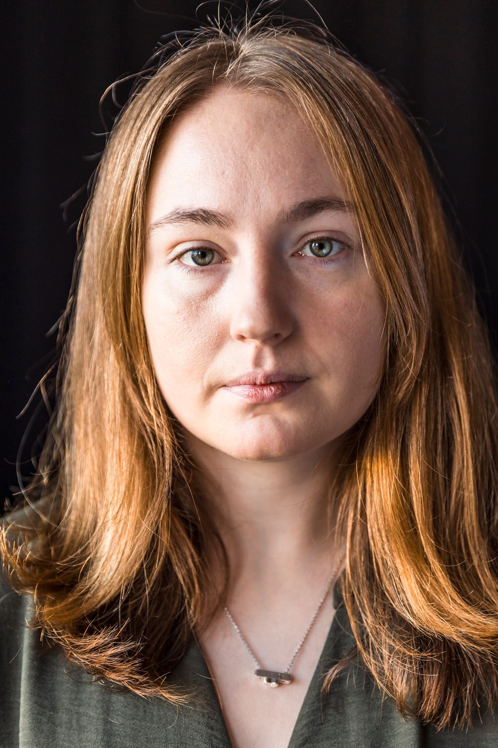 Portrait of a young woman with long auburn hair and green eyes wearing a green shirt and delicate bar necklace.