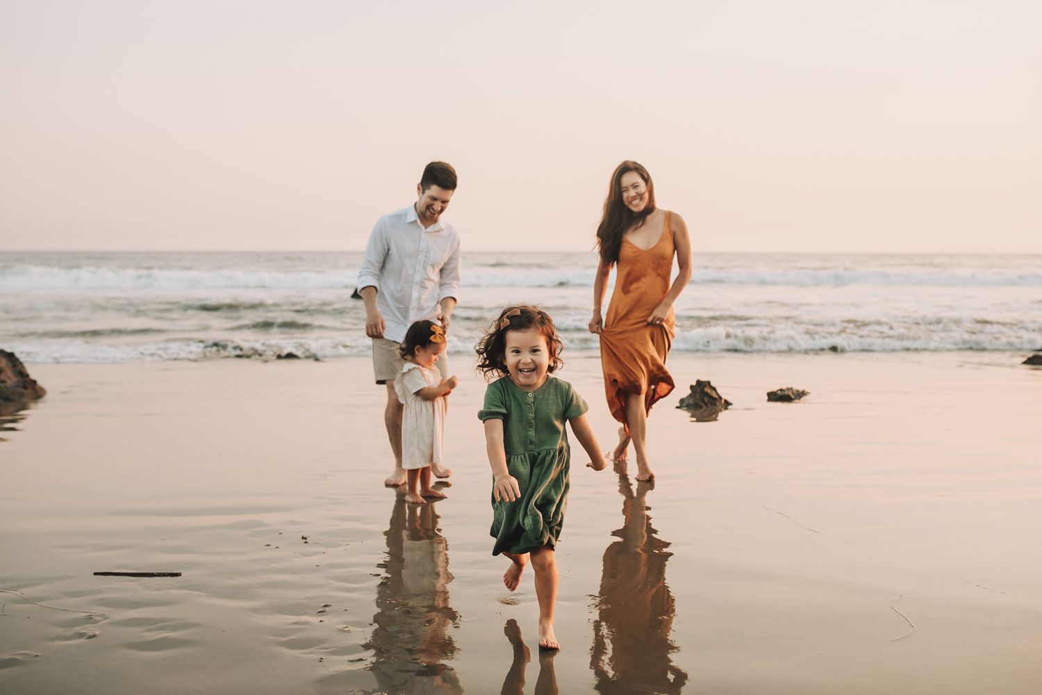 A group walks along the beach during sunset, leaving footprints in the sand as waves roll in from the ocean.