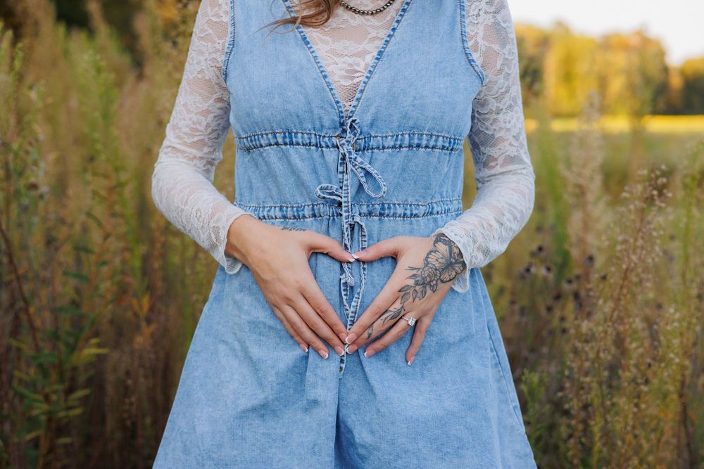 A person wearing a denim dress stands in a golden field at sunset with wildflowers and tall grass.