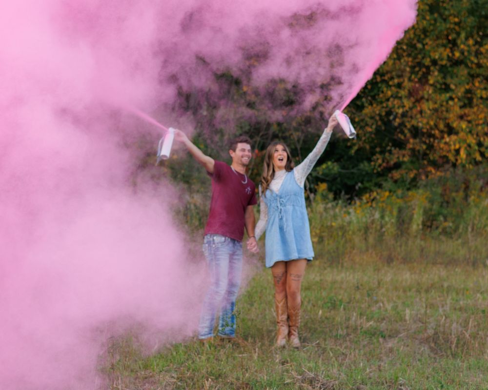 People celebrate in a field with vibrant pink smoke bombs creating a dramatic colorful effect in nature.