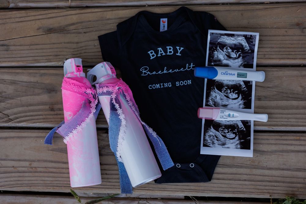 A pregnancy announcement display with baby shoes, ultrasound photos, and a black t-shirt laid on wooden planks.