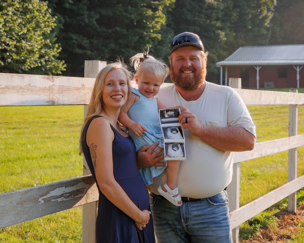 A family stands together outdoors by a white fence during a golden sunset photo session.