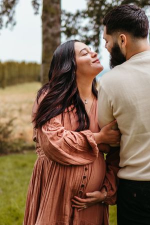 A romantic couple embraces outdoors in a field with soft lighting and natural scenery.