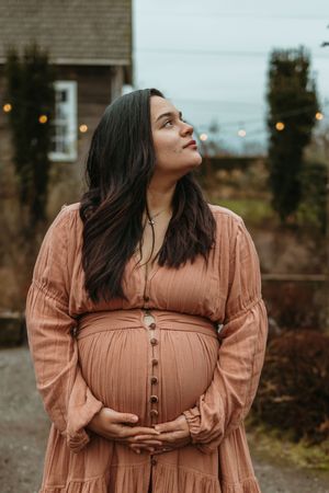 A person in a peach-colored button-up dress poses outdoors against a moody backdrop in a photo series.