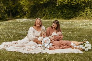 A peaceful outdoor family photoshoot on a white blanket in a grassy field with soft natural lighting.
