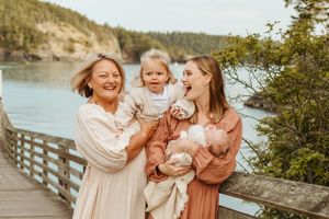 Three people share joyful moments together on a wooden boardwalk overlooking a scenic waterfront landscape.