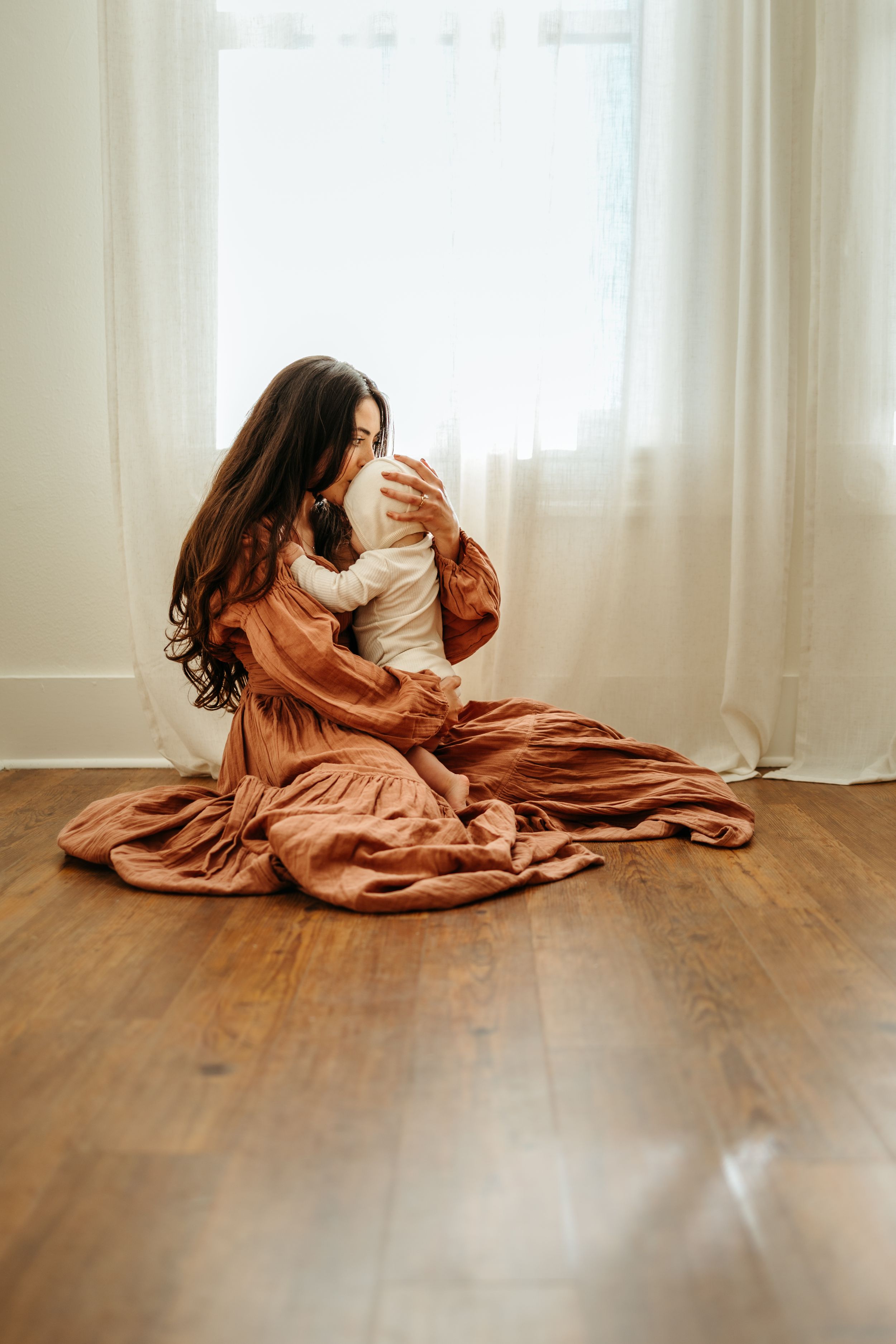 A series of artistic photographs showing a person in flowing terracotta fabric lying on wooden floor near white curtains.