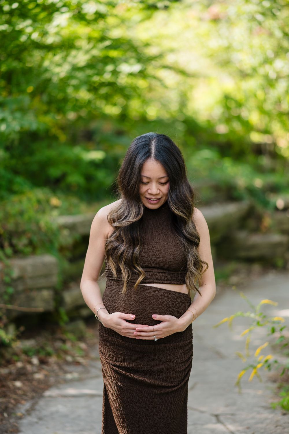 A maternity photo series shows a pregnant woman in a brown dress outdoors in a natural garden setting.