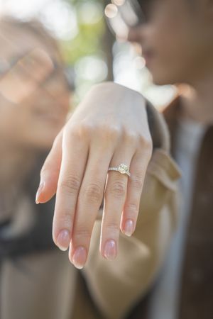 A hand wearing an engagement ring showcases a sparkling diamond in natural light.