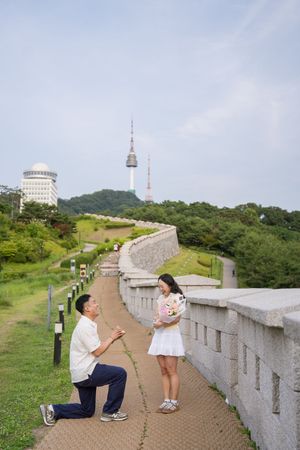 Proposal moment on pathway near Seoul Tower with stone walls and greenery.