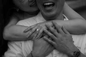 Black and white intimate photo of couple embracing with ring visible.