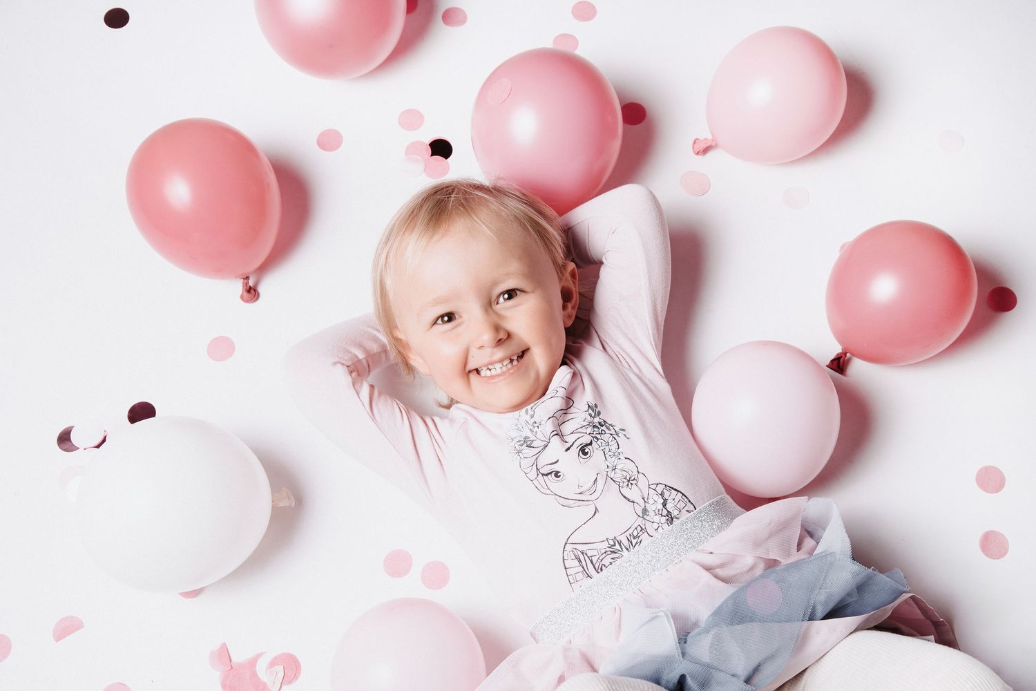 Foto in einem Fotostudio in Gelsenkirchen Hassel. Mädchen liegt auf dem Rücken mit rosa Luftballons beim Fotoshootings mit Kinderfotograf