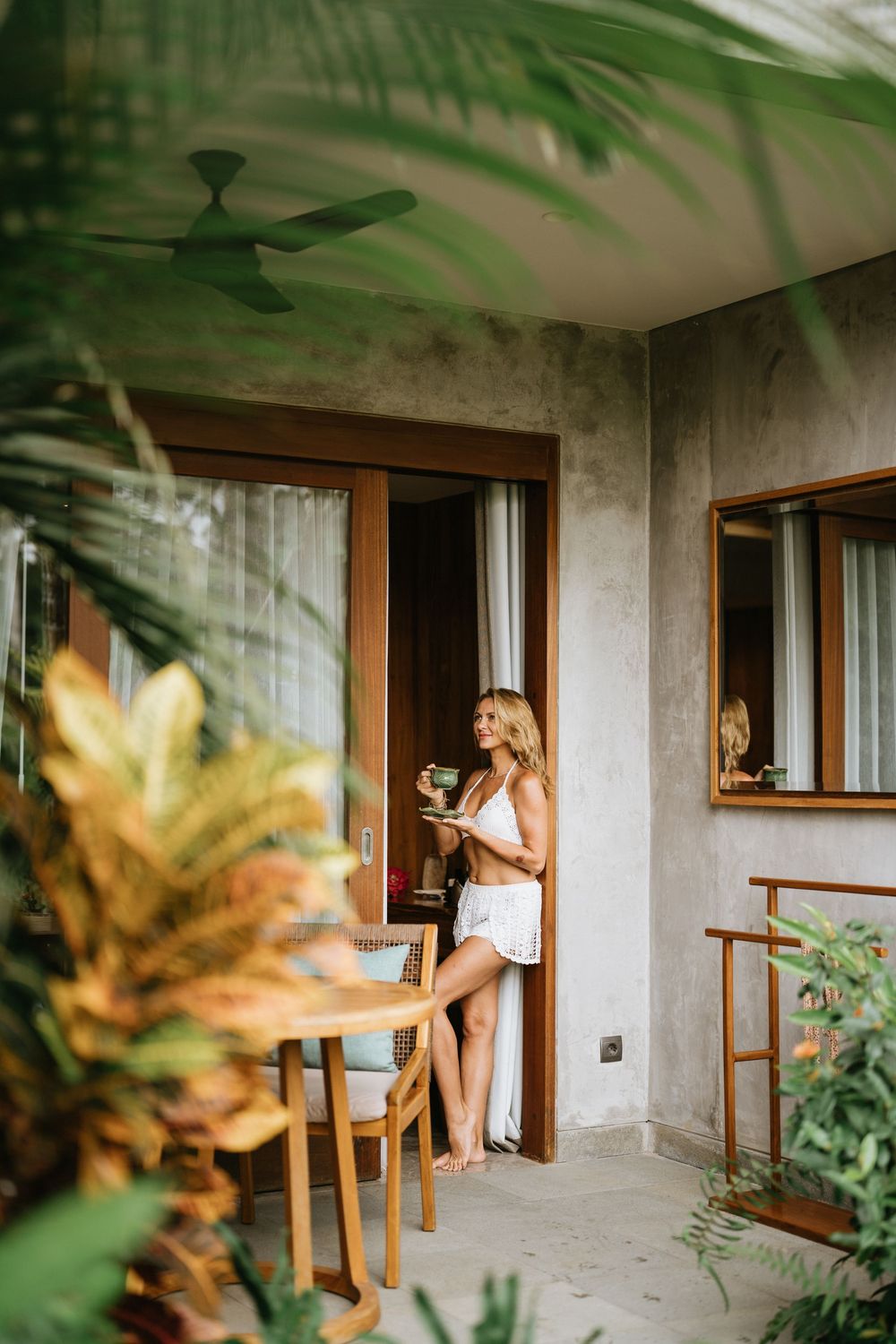 A tropical balcony scene with palm fronds and wooden furniture creating a relaxing resort atmosphere.
