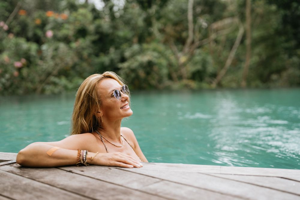 Relaxing scene at an infinity pool with turquoise water surrounded by tropical forest.