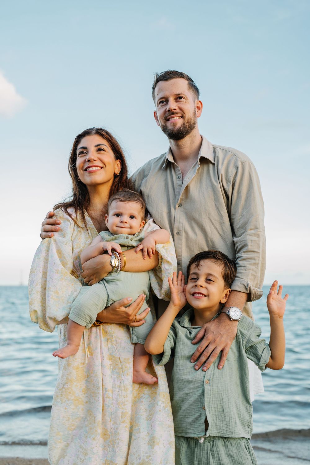 A cheerful family poses together against a beautiful ocean backdrop.