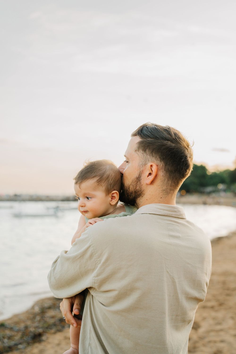 Parent and child share tender moments while watching the sunset at the beach.