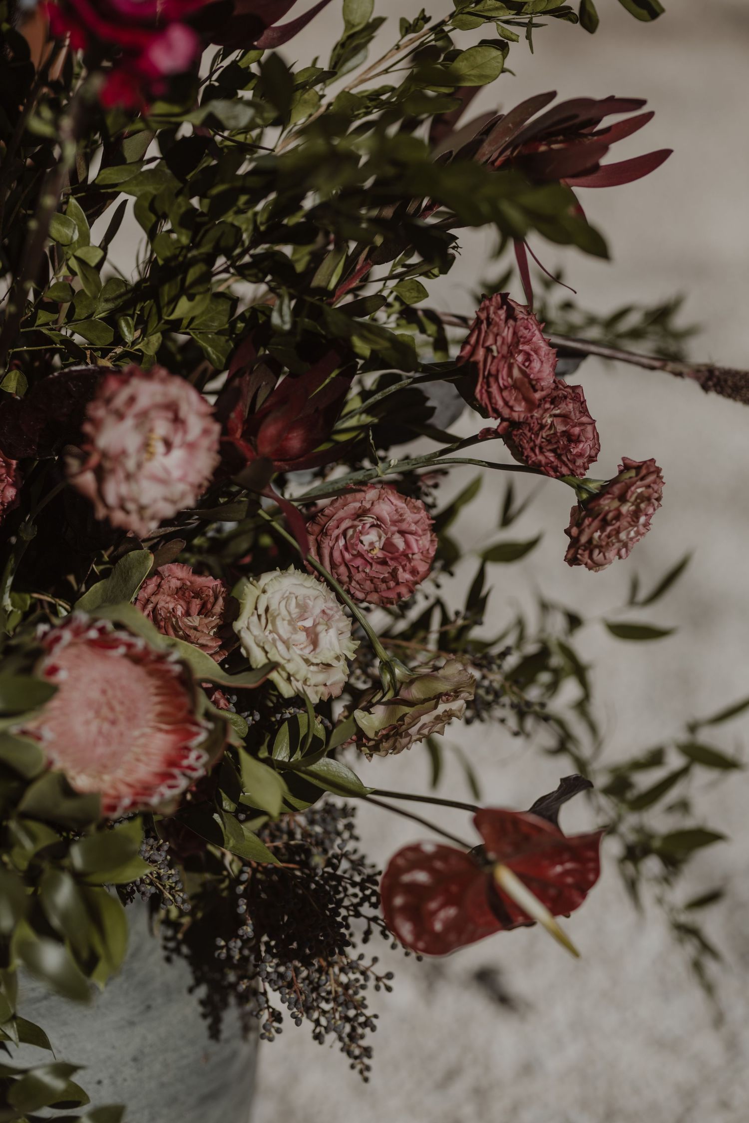 Moody floral arrangement with pink roses and burgundy blooms against a neutral background.