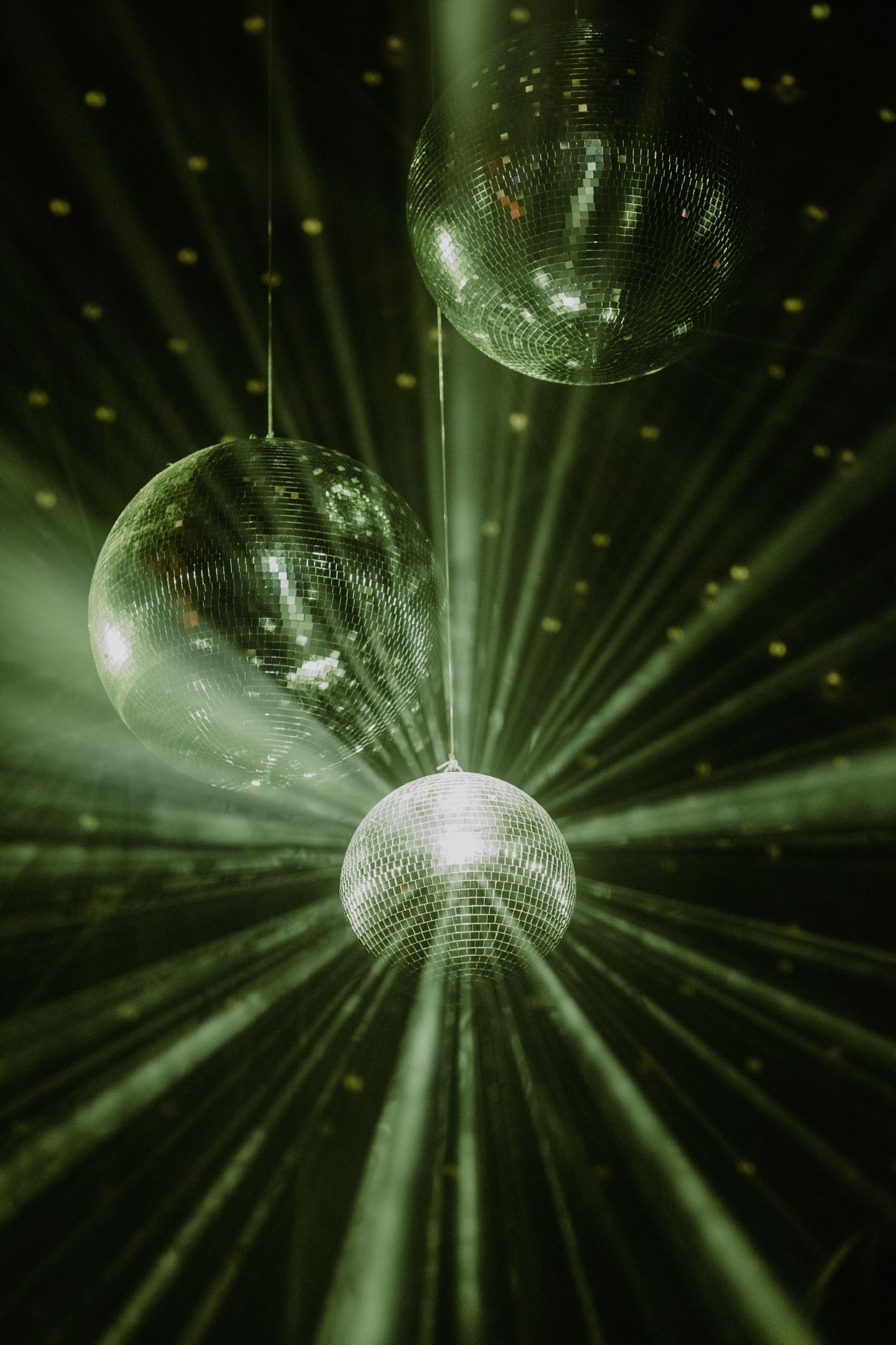 A rotating disco ball reflects sparkling green light beams in a dark nightclub atmosphere.