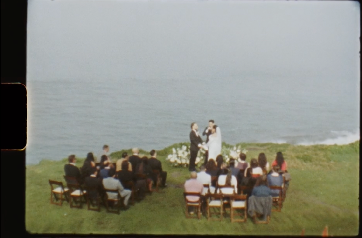 Wedding reception guests enjoying drinks and conversation at dimly lit table.