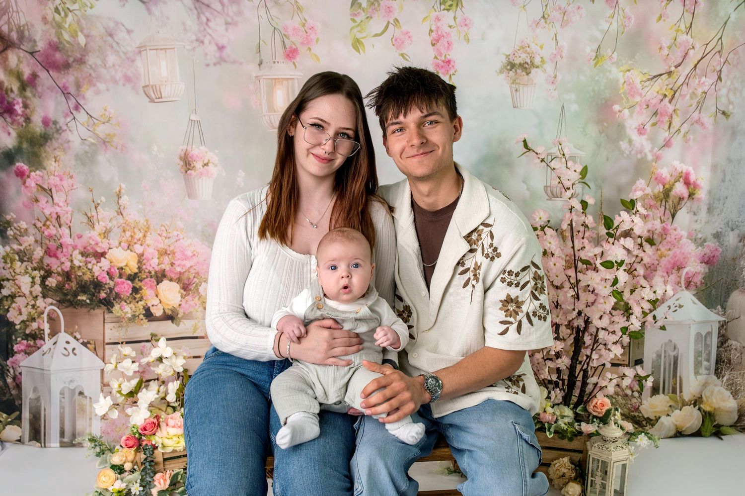 Family wearing coordinated blue outfits poses together with green plants against white brick wall.
