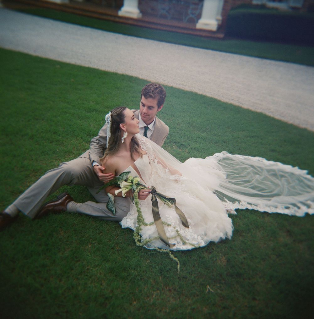 Couple poses intimately on lush green lawn during golden hour wedding photography session.
