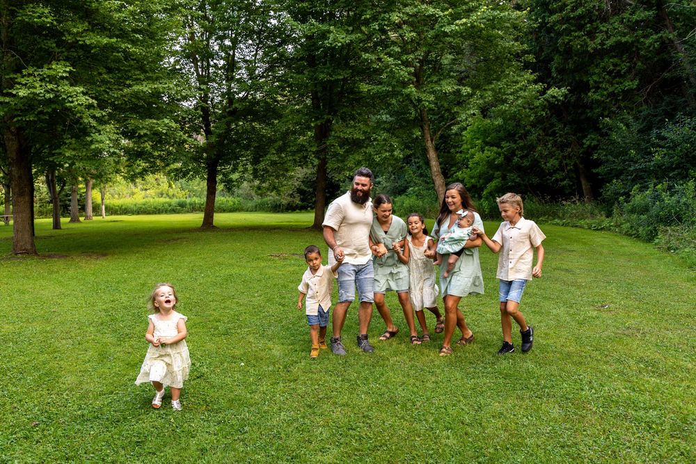 Family of 8 all squished closer together with the second youngest child off to the side looking into the distance