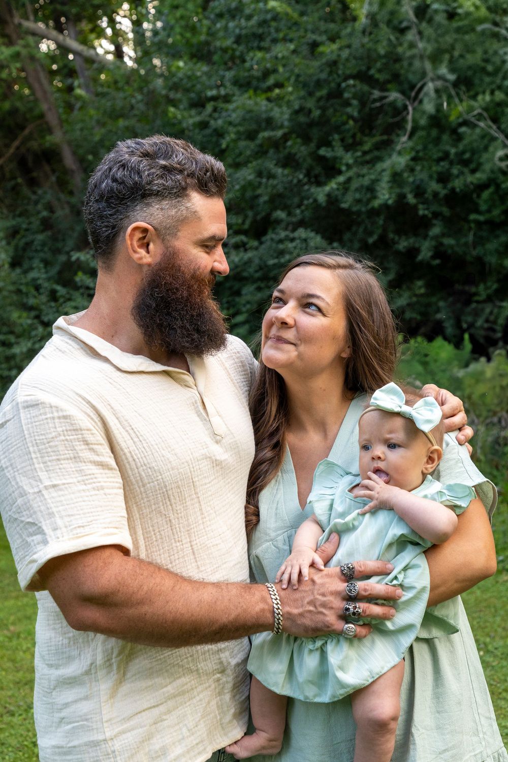 A mother holding her baby gazing at her husband next to her as he places his hand on their baby
