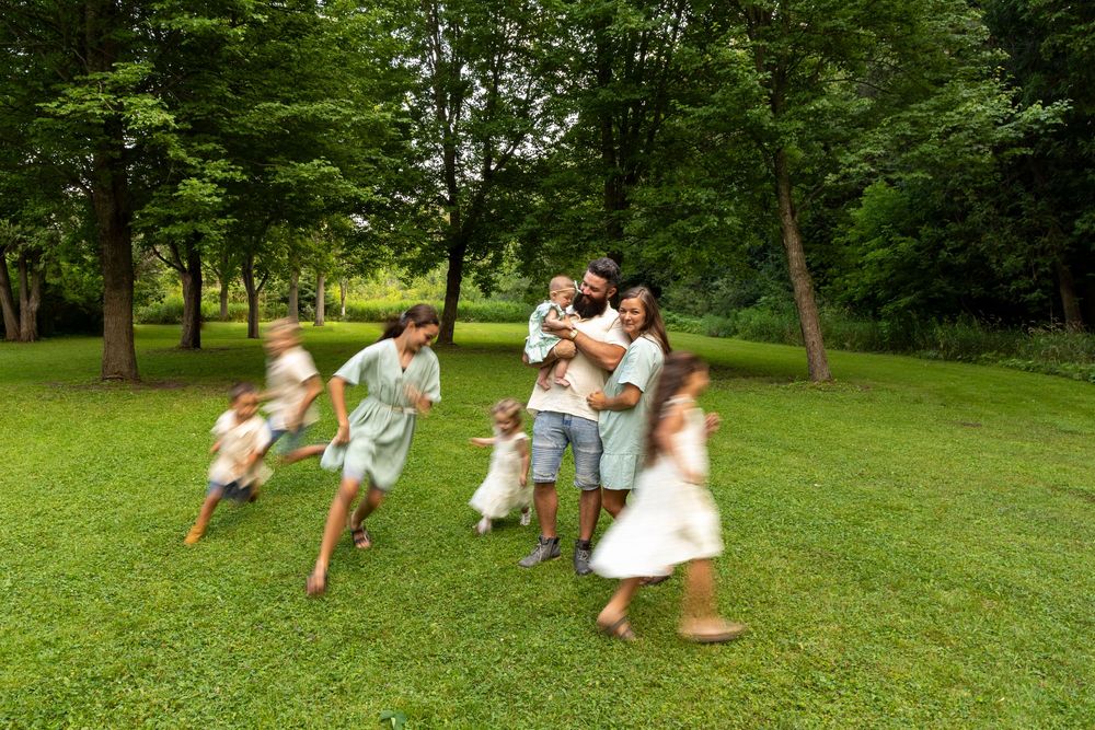 A mom, dad and baby hugging in a park with their 5 additional children running around them (blurred)