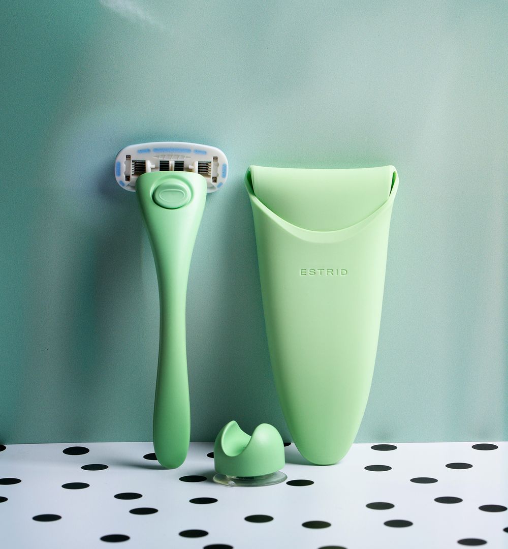 Mint green razor and holder set against turquoise background with polka dot surface.