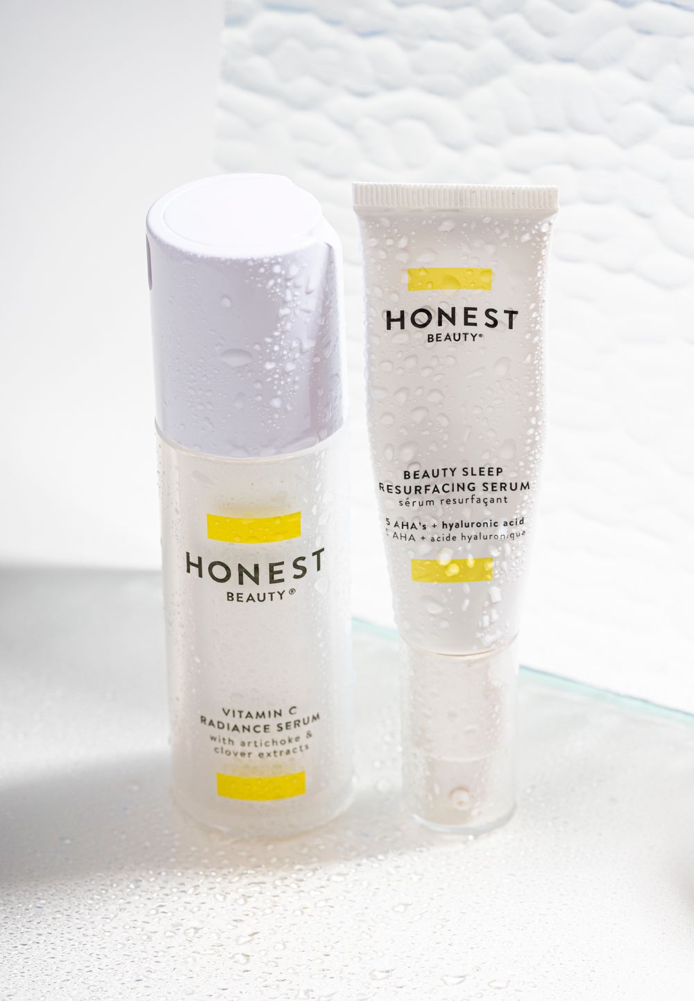 Honest Beauty skincare products displayed on white textured surface with water droplets.