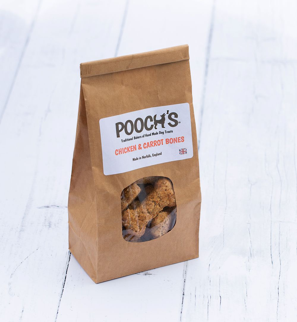 Three brown paper bags containing dog treats labeled Pooch's on white wooden background.