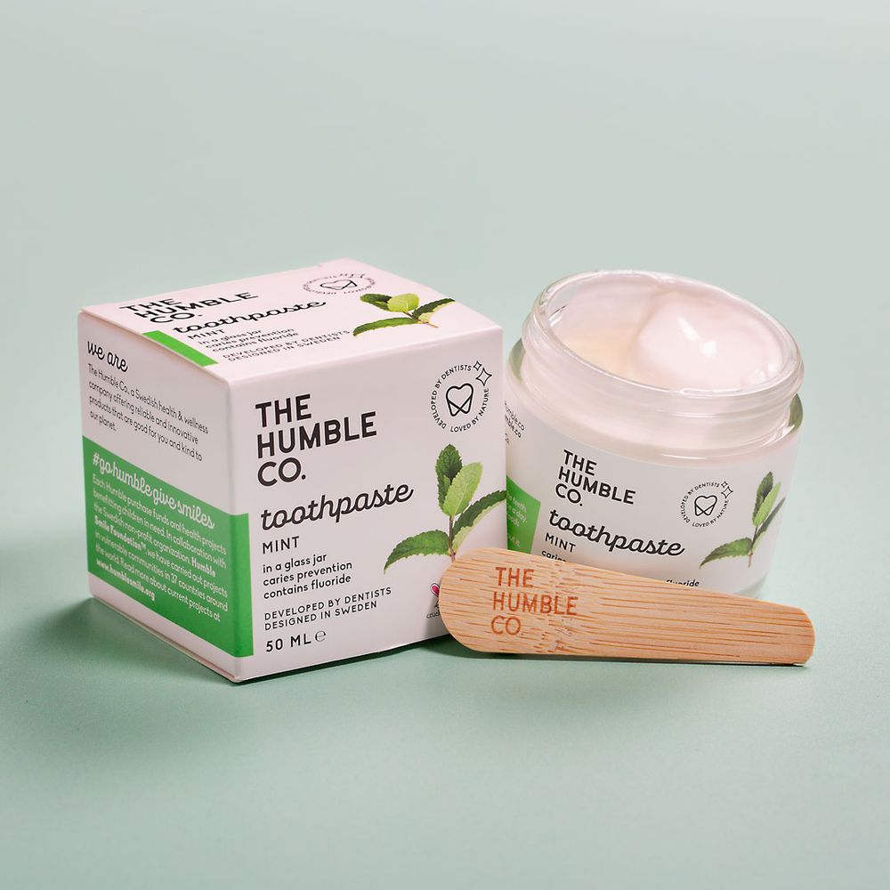 Eco-friendly toothpaste packaging with wooden applicator and natural-looking cream product.