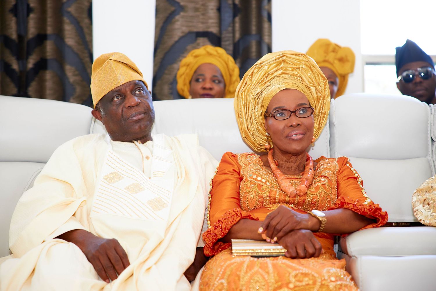 Colorful traditional Nigerian celebration with guests wearing bright orange and gold attire seated in white chairs.