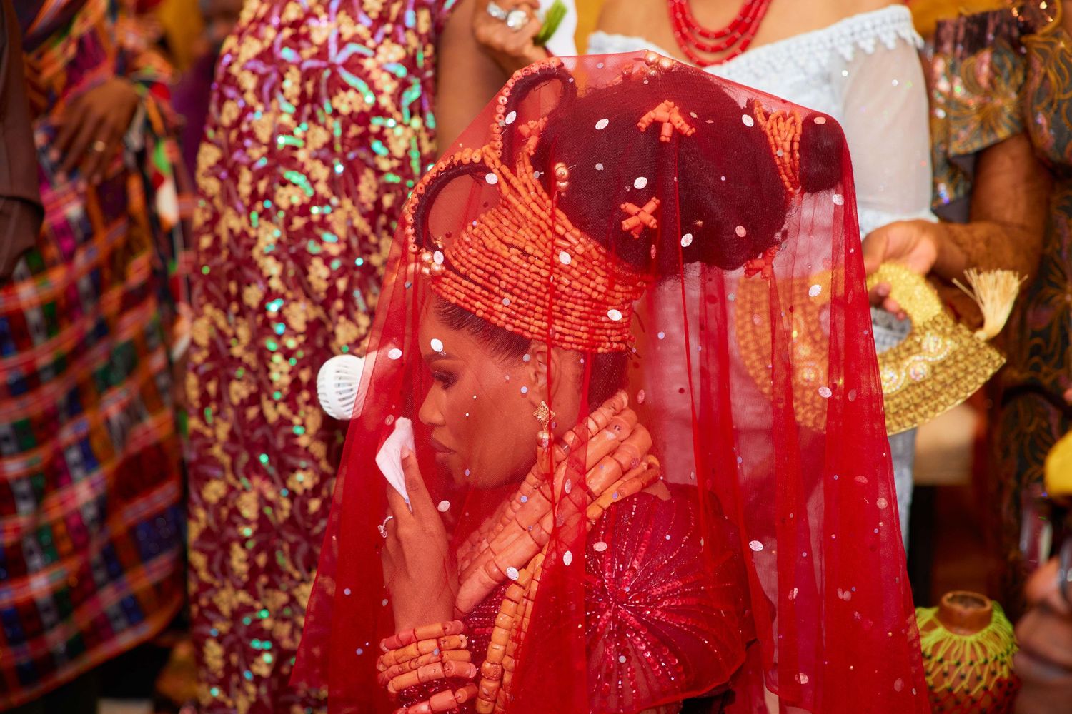 Traditional ceremony with a participant wearing bright red attire and veil adorned with ornate jewelry and accessories.