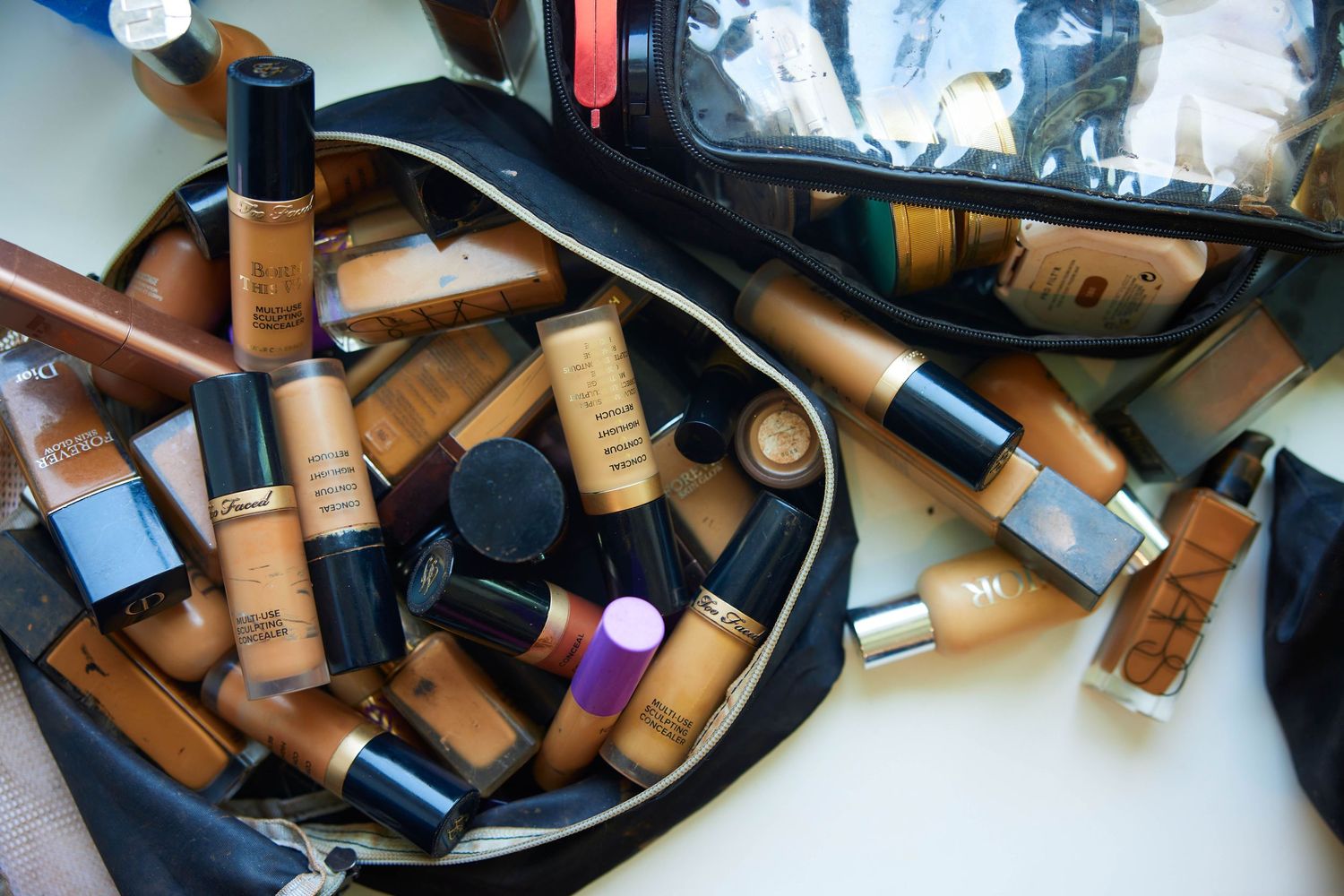 Scattered pile of various lipstick tubes and makeup items on a white surface creating a messy beauty product display.