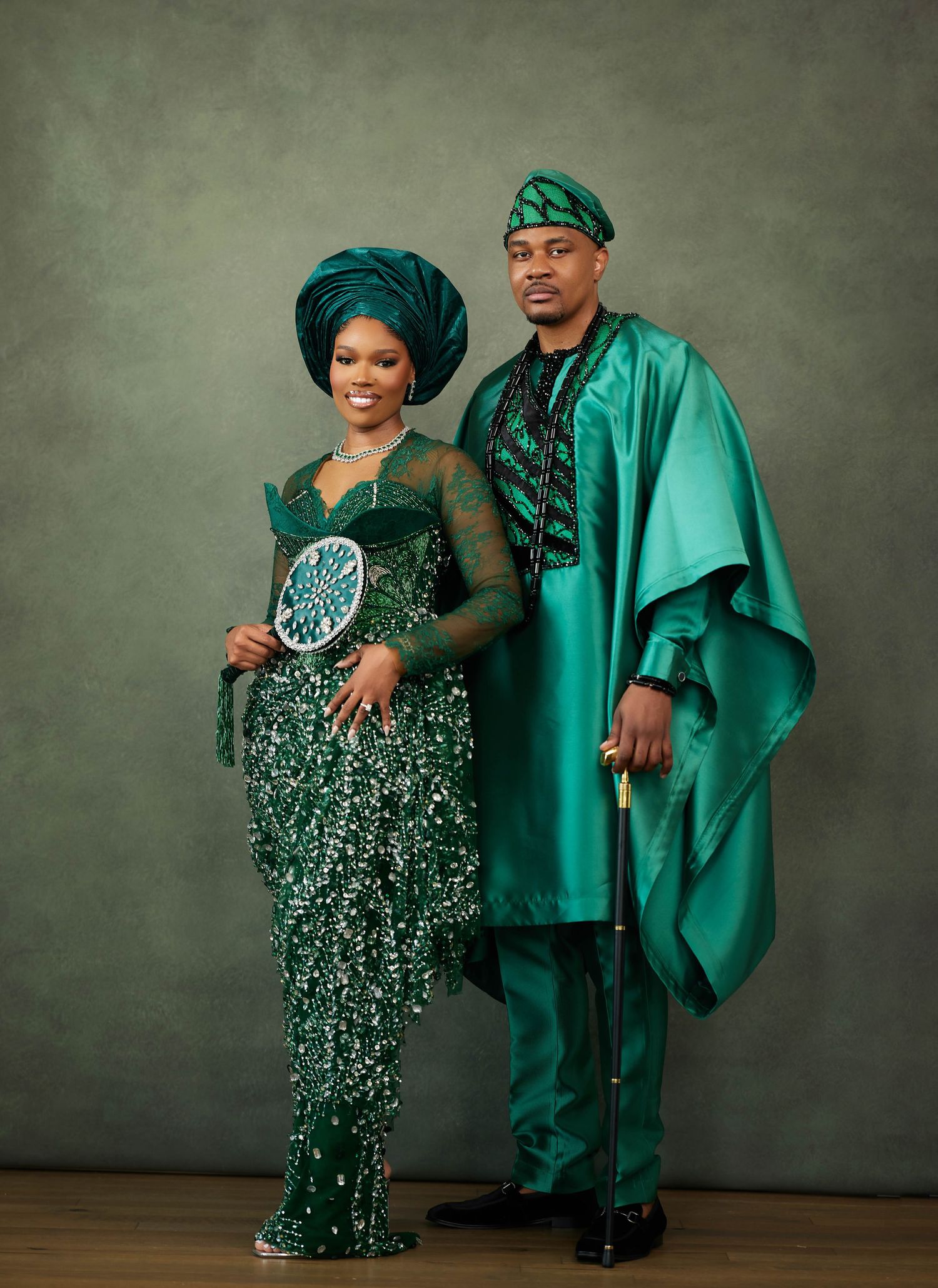 African couple poses together in elegant emerald green matching outfits with sparkly details for formal portraits.