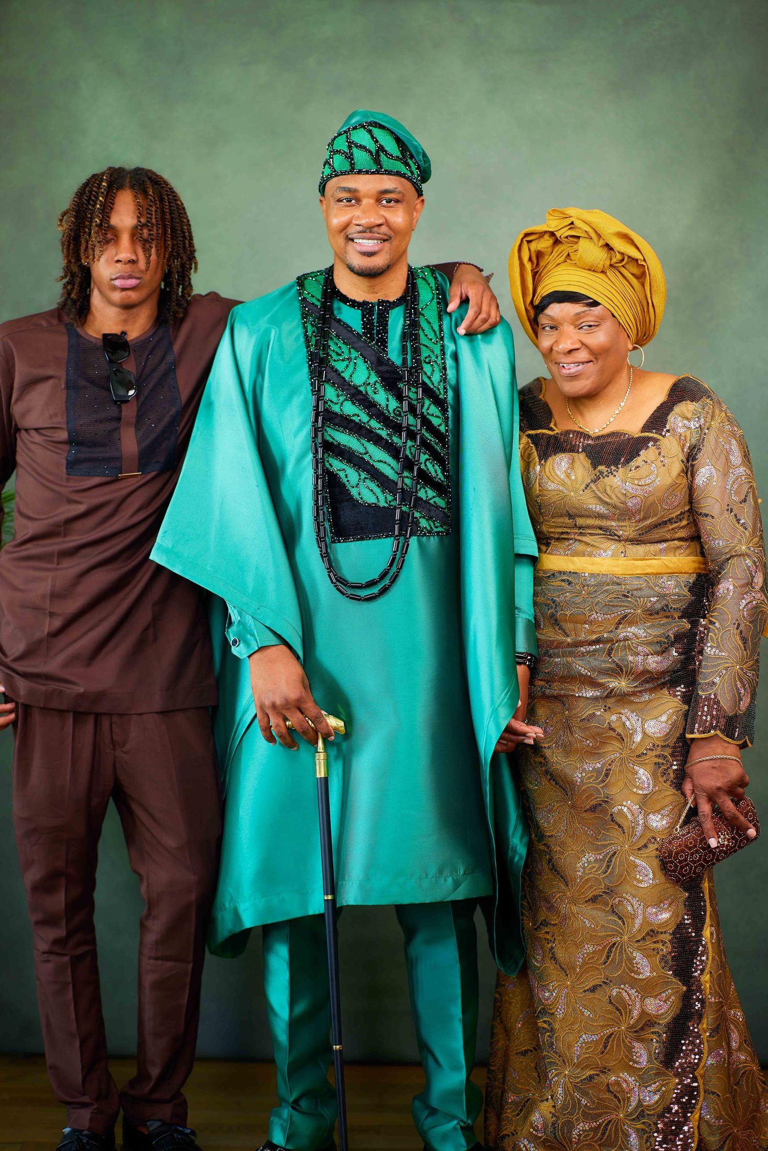 Family photoshoot features matching traditional Nigerian outfits in turquoise and golden brown against studio backdrop.