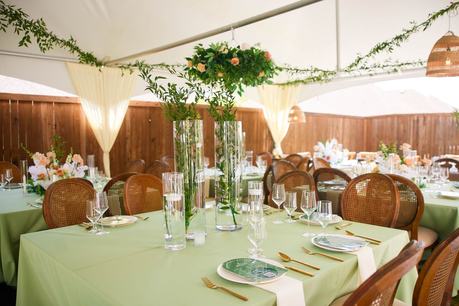 Elegant wedding reception venue setup with round tables and white linens under a draped tent ceiling with hanging greenery.
