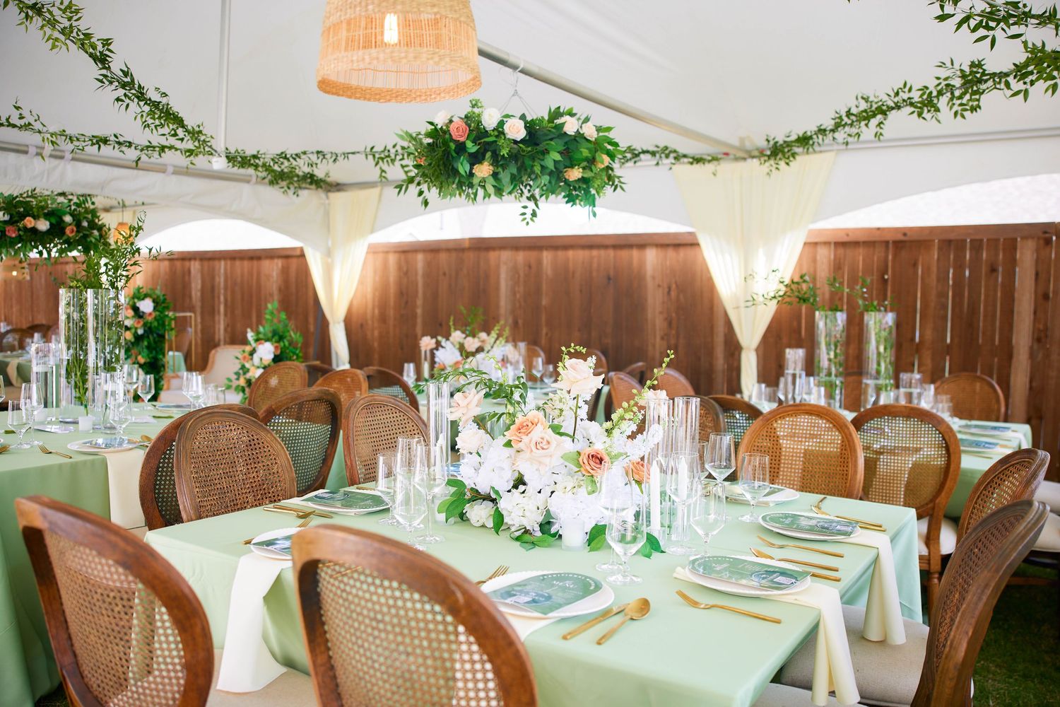 Elegant wedding reception venue with greenery decorations, white linens, and cane back chairs in a rustic-chic setting.