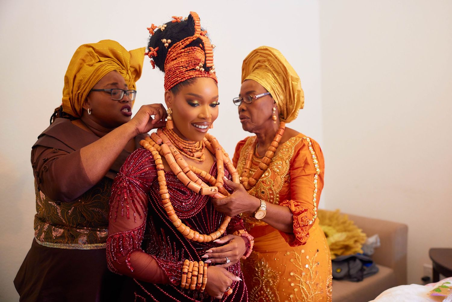 Two people in traditional African attire share an intimate moment during a wedding ceremony in burgundy and gold outfits.