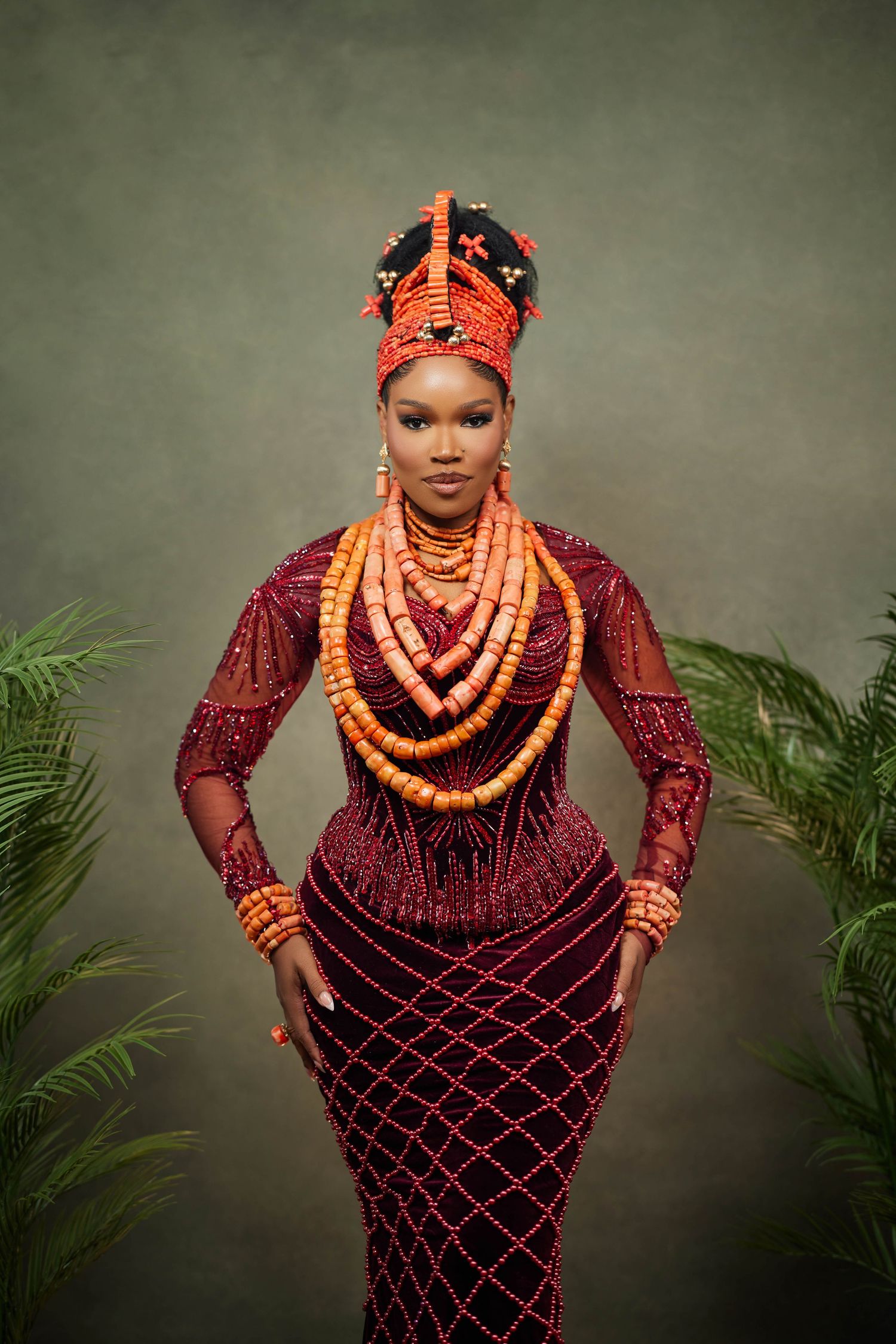 Traditional Nigerian Edo bride wearing deep burgundy dress with coral beaded jewelry and headdress in a studio portrait series.
