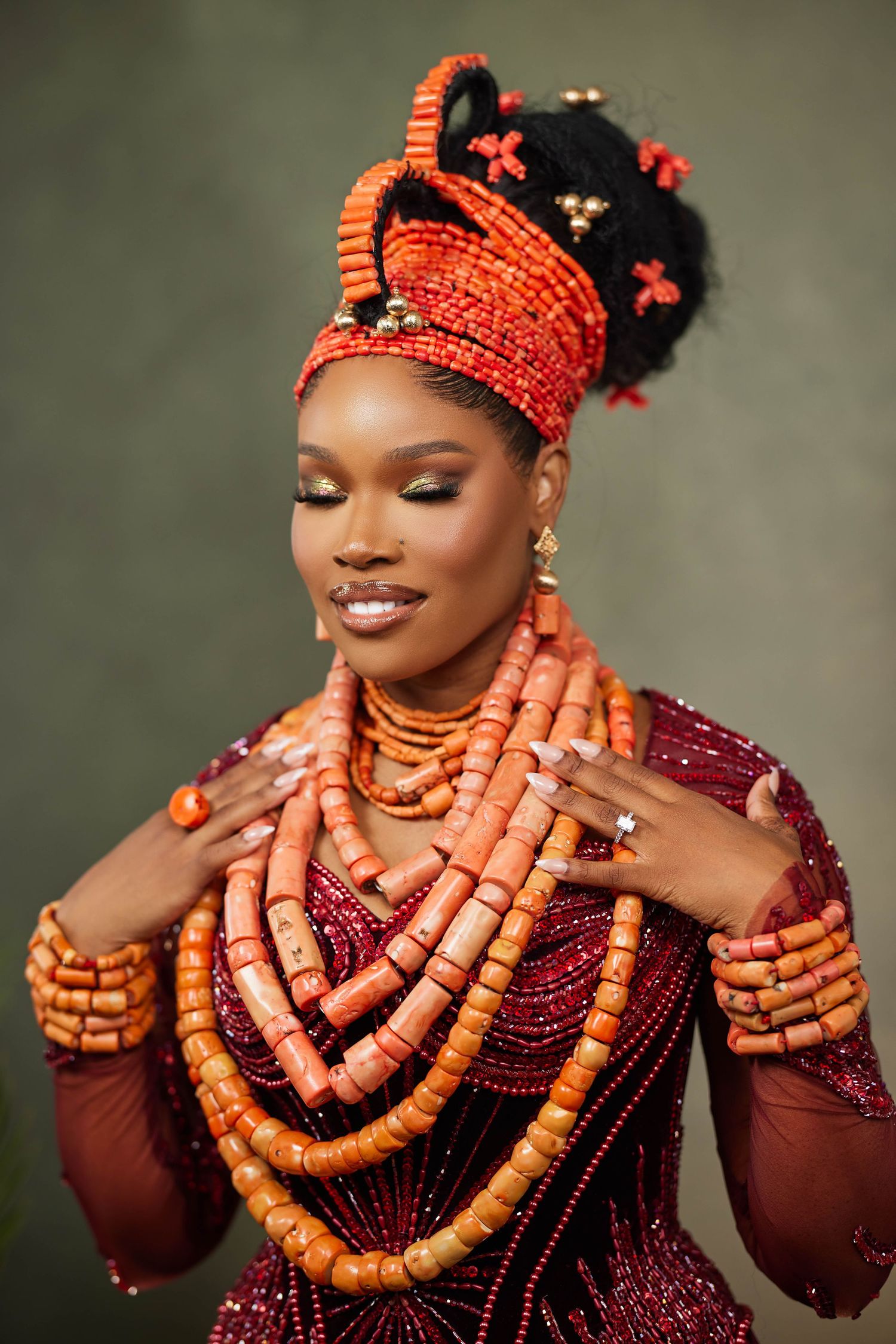 Traditional Nigerian bride adorned in luxurious coral beaded necklaces and burgundy attire shows off elegant jewelry.