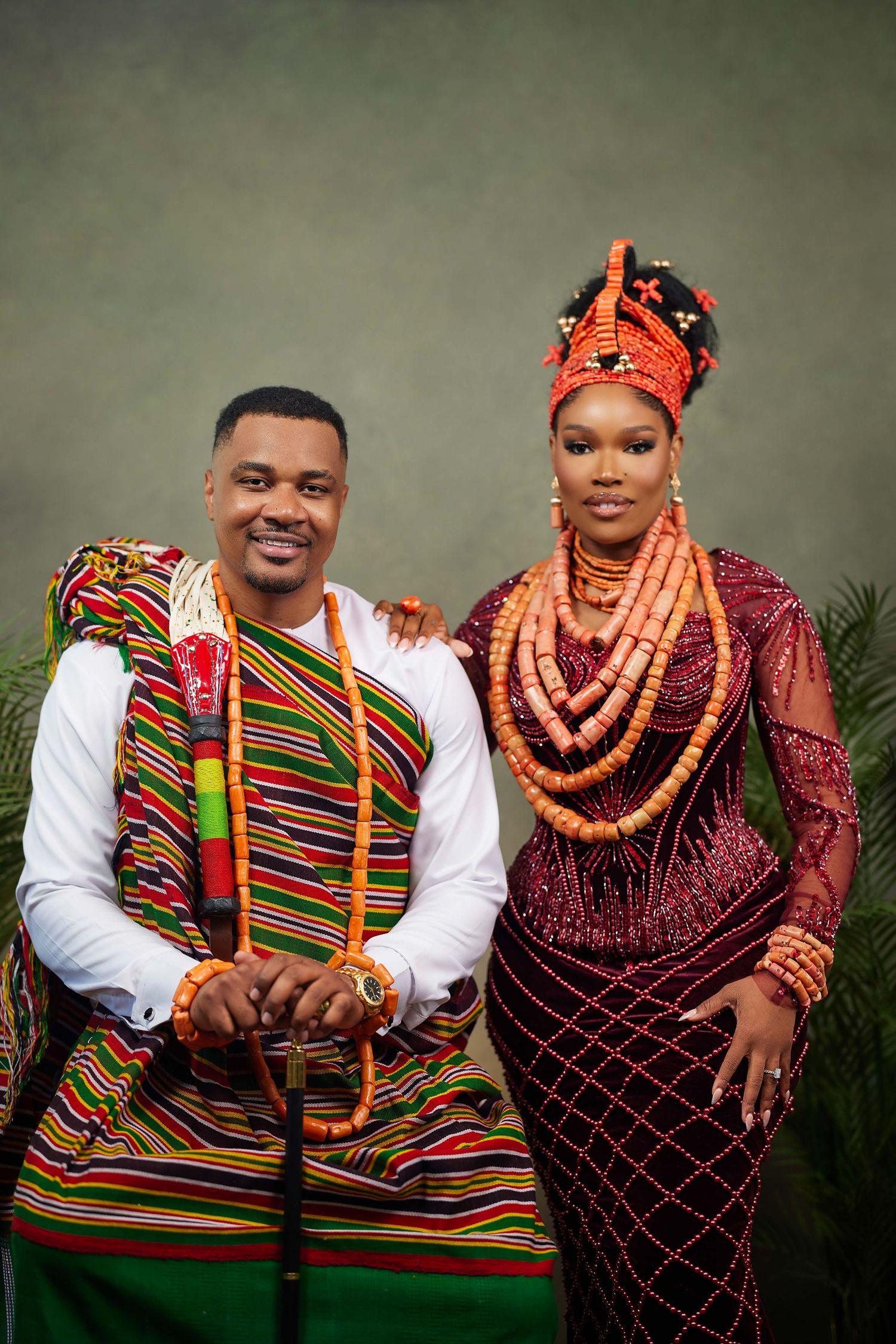 Traditional Nigerian couple pose in vibrant cultural attire with colorful beads and festive fabrics.
